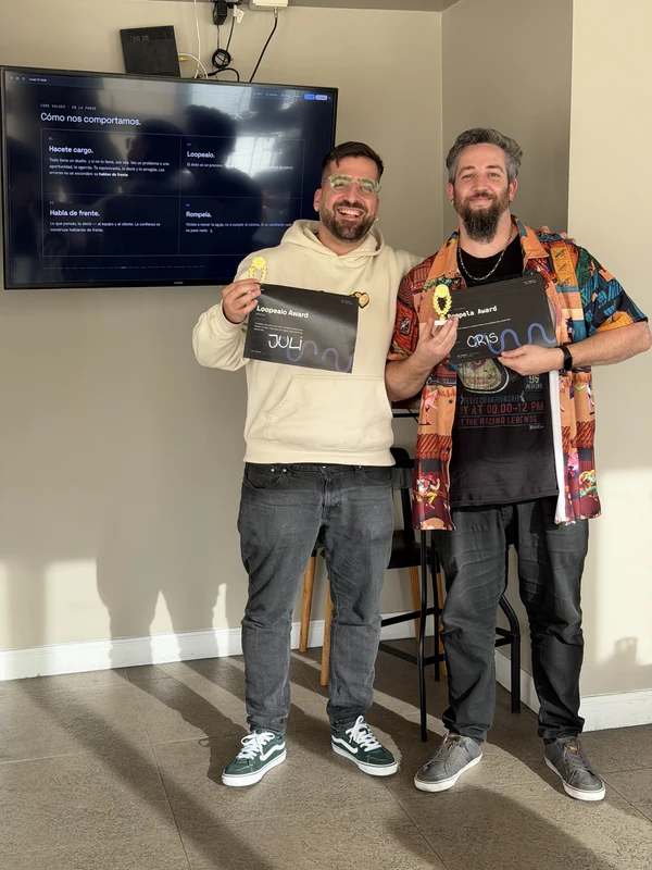 Two teammates holding a framed award in front of a presentation screen